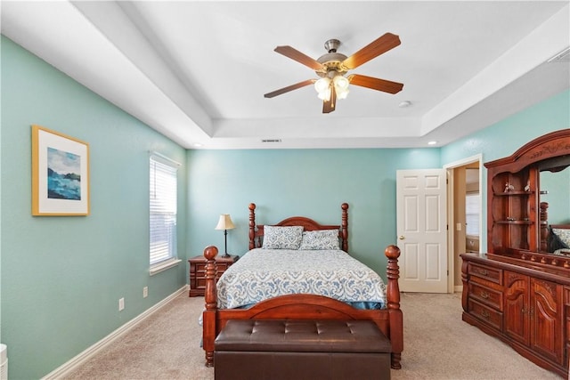 bedroom with a raised ceiling, ceiling fan, and light colored carpet