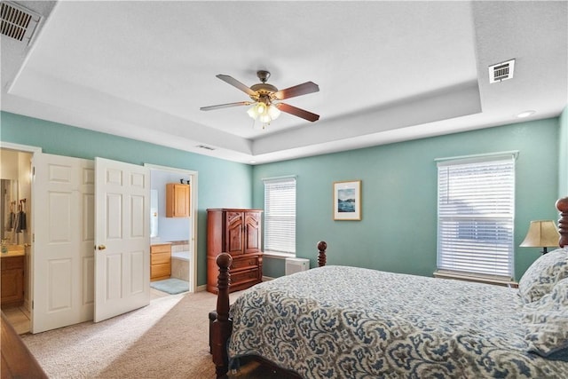 bedroom featuring ceiling fan, multiple windows, a tray ceiling, and ensuite bath