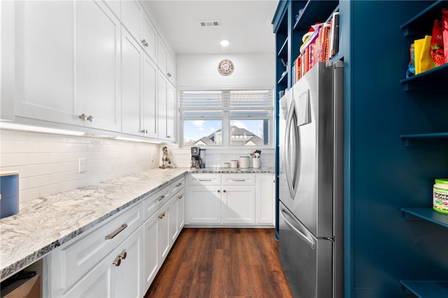 kitchen featuring decorative backsplash, white cabinets, light stone countertops, and freestanding refrigerator