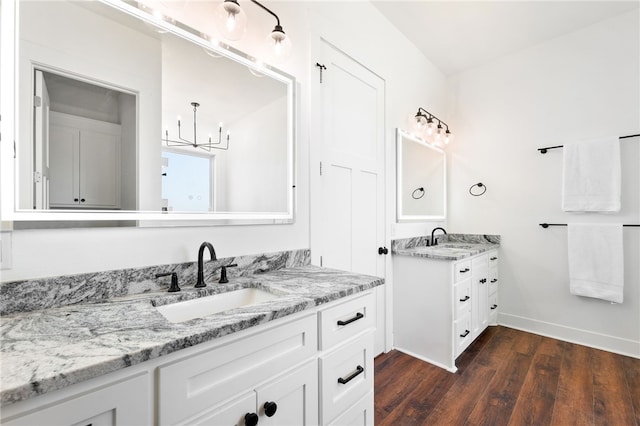 full bath featuring wood finished floors, two vanities, baseboards, and a sink