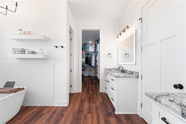 full bathroom featuring a soaking tub, vanity, a walk in closet, and wood finished floors