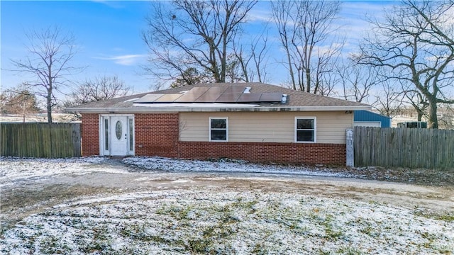 snow covered back of property featuring solar panels