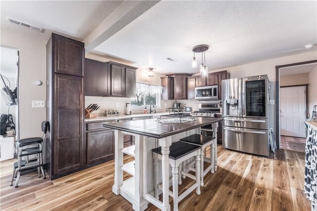 kitchen featuring appliances with stainless steel finishes, dark brown cabinets, decorative light fixtures, light hardwood / wood-style flooring, and a center island