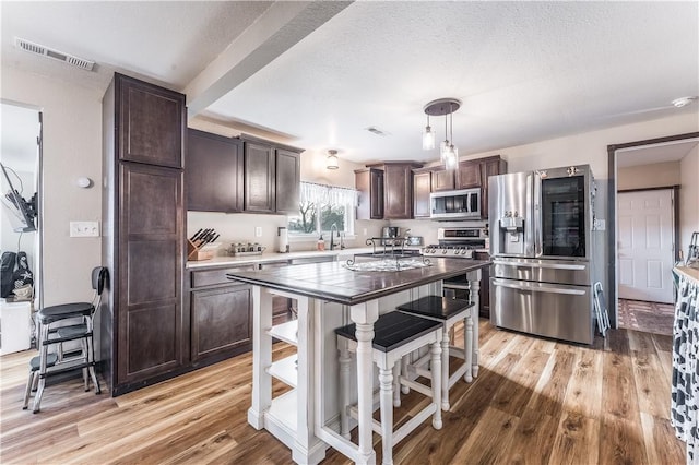 kitchen with decorative light fixtures, a center island, dark brown cabinets, light hardwood / wood-style flooring, and appliances with stainless steel finishes