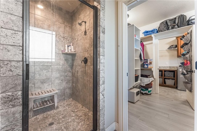 bathroom featuring a spacious closet, a shower stall, and wood finished floors