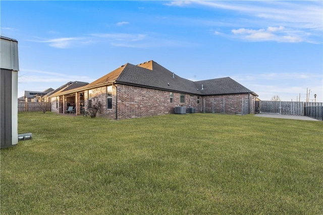 back of house featuring a patio, central AC unit, a fenced backyard, brick siding, and a lawn