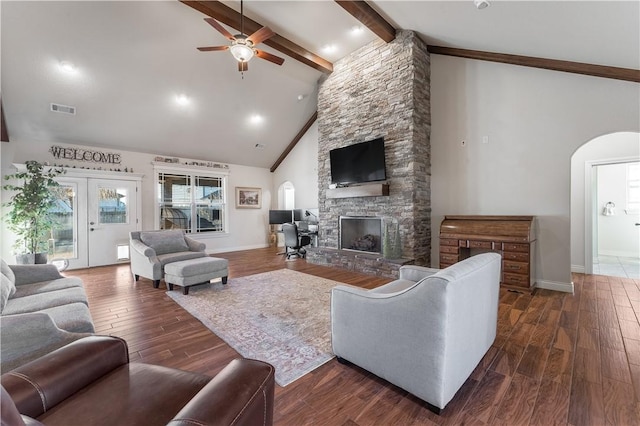 living area with dark wood-style floors, arched walkways, visible vents, a stone fireplace, and beamed ceiling