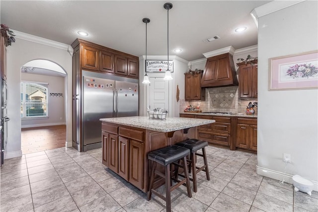 kitchen with custom range hood, a kitchen island, ornamental molding, decorative light fixtures, and stainless steel appliances