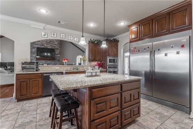 kitchen featuring built in appliances, visible vents, open floor plan, a center island, and decorative light fixtures