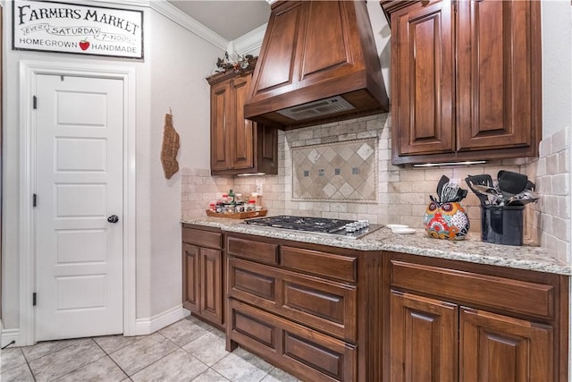 kitchen featuring light tile patterned floors, custom range hood, light stone counters, crown molding, and stainless steel gas cooktop