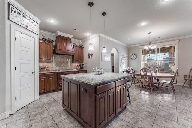 kitchen with arched walkways, pendant lighting, stainless steel gas stovetop, a kitchen island, and premium range hood