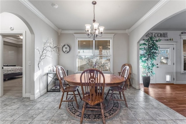 dining room featuring arched walkways, a chandelier, light wood-style flooring, baseboards, and crown molding