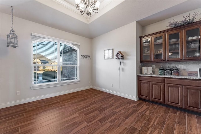 unfurnished dining area with dark wood-type flooring, a tray ceiling, a chandelier, and baseboards