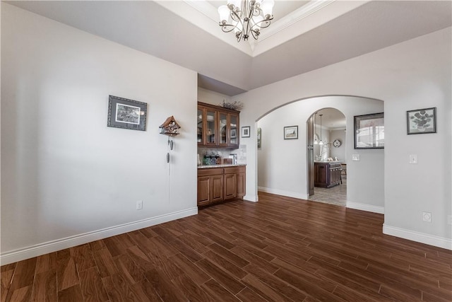 bar featuring arched walkways, a notable chandelier, baseboards, hanging light fixtures, and dark wood-style floors