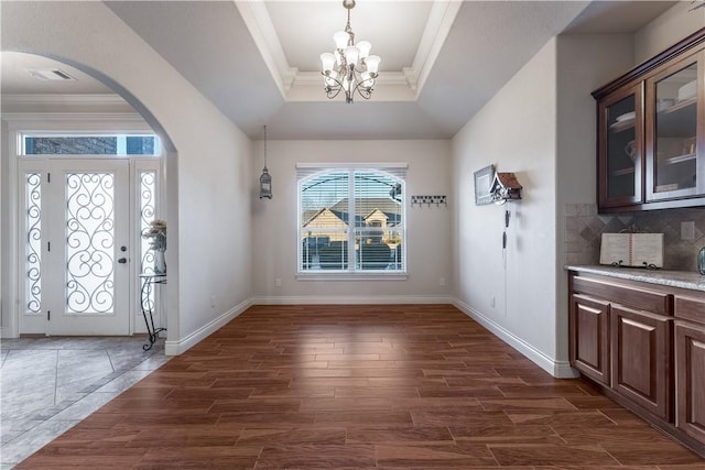 foyer with dark wood-type flooring, arched walkways, a raised ceiling, and crown molding