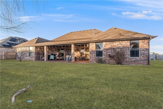 rear view of house featuring a lawn, roof with shingles, fence, a patio area, and brick siding