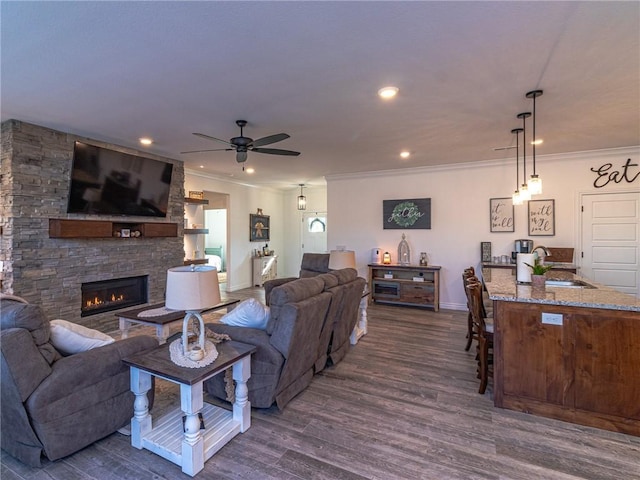 living room featuring sink, ceiling fan, dark hardwood / wood-style floors, ornamental molding, and a fireplace