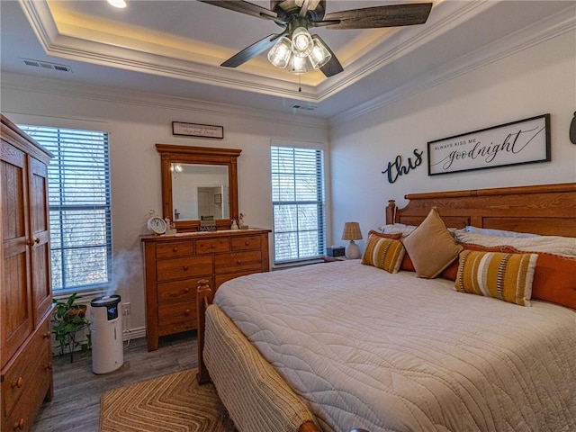 bedroom with multiple windows, a tray ceiling, ceiling fan, and dark wood-type flooring