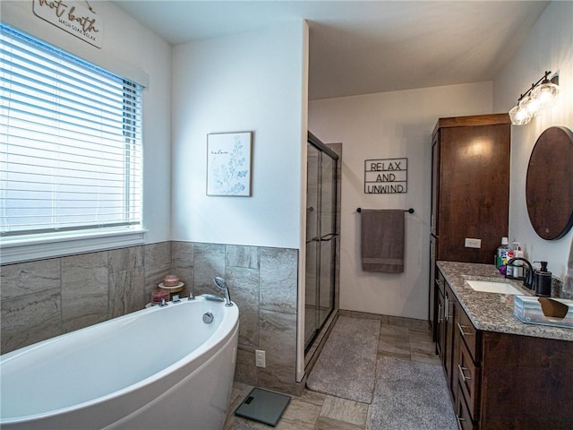 bathroom with vanity, independent shower and bath, tile walls, and a healthy amount of sunlight