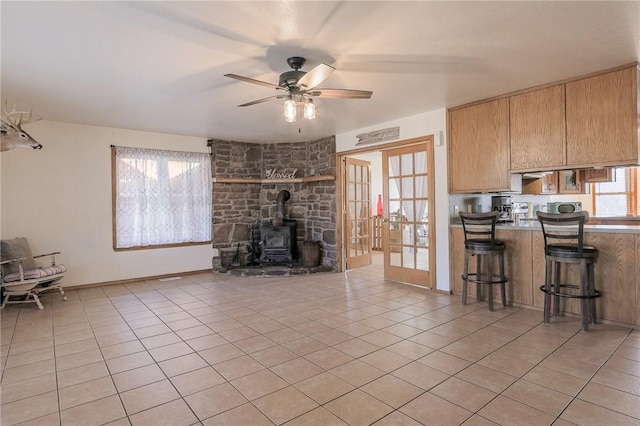 unfurnished living room with french doors, a wood stove, ceiling fan, and light tile patterned flooring