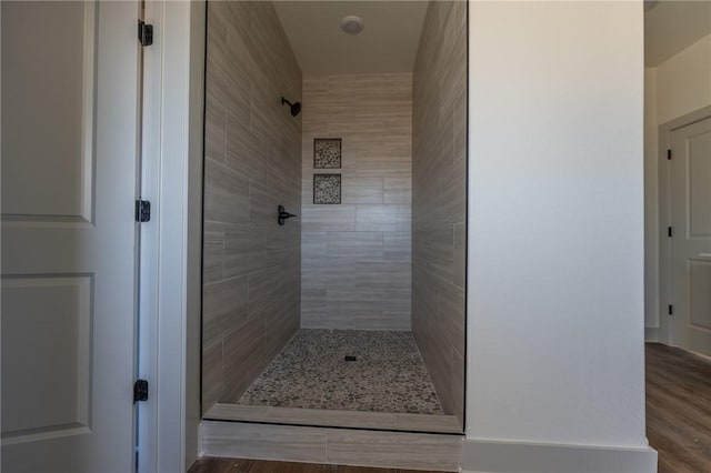 bathroom with a tile shower and wood-type flooring