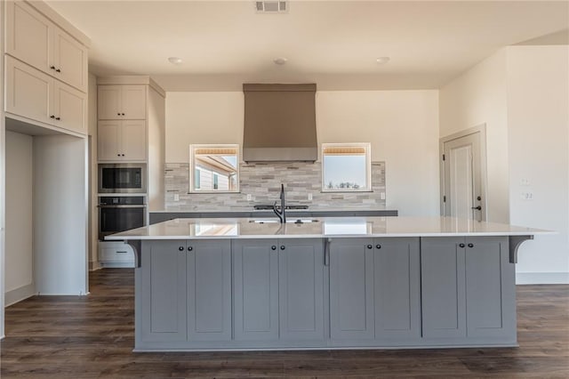 13121 Bethel Blacktop Rd, Farmington, AR 72730 - kitchen featuring a center island with sink, appliances with stainless steel finishes, wall chimney exhaust hood, light countertops, and decorative backsplash