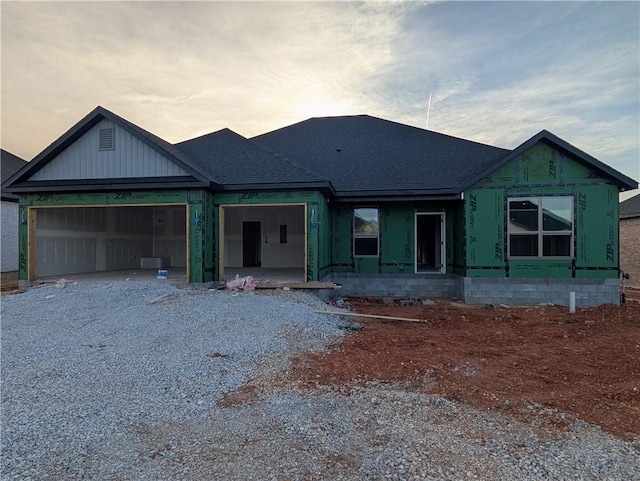 unfinished property featuring driveway, a garage, and roof with shingles