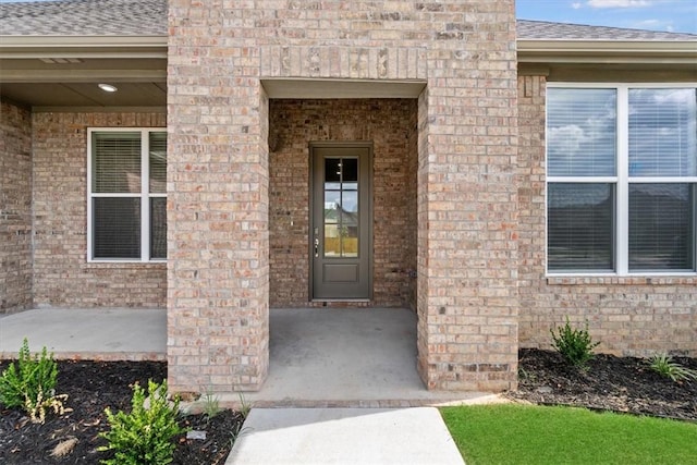 entrance to property with brick siding and a shingled roof