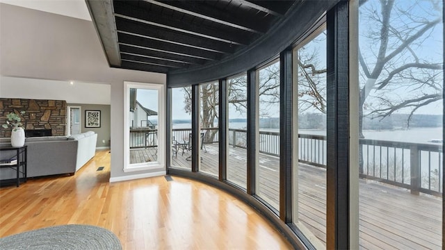 sunroom featuring beam ceiling, a stone fireplace, and a water view