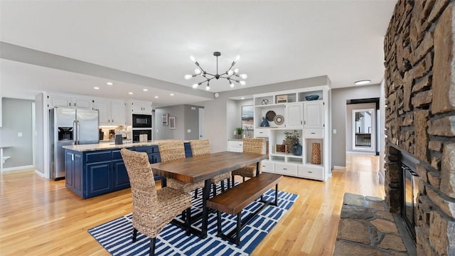 dining space featuring built in shelves, a fireplace, a chandelier, and light hardwood / wood-style floors