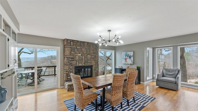 dining area with a healthy amount of sunlight, a fireplace, a chandelier, and light hardwood / wood-style flooring