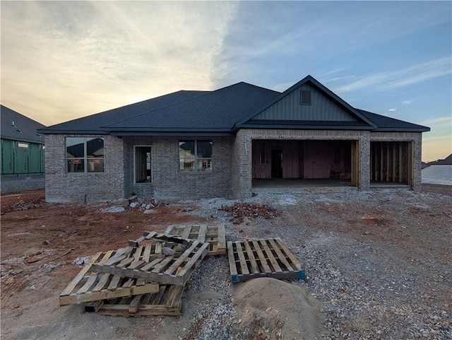 back of property featuring driveway, board and batten siding, roof with shingles, an attached garage, and brick siding