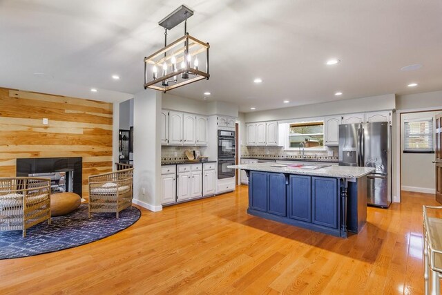 kitchen with stainless steel refrigerator with ice dispenser, black double oven, light hardwood / wood-style floors, decorative light fixtures, and white cabinets