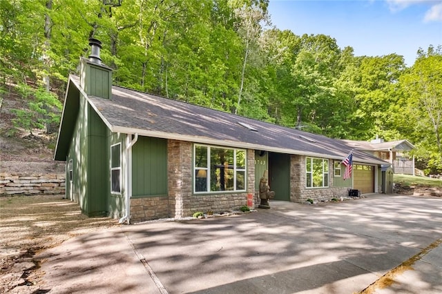 view of front of home featuring a garage, driveway, stone siding, a chimney, and roof with shingles