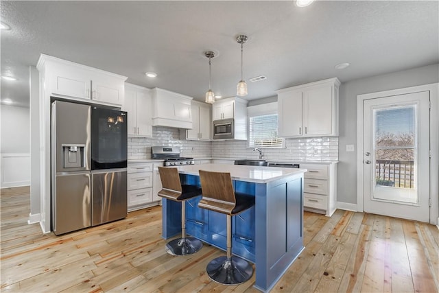 kitchen featuring white cabinets, appliances with stainless steel finishes, a center island, and pendant lighting