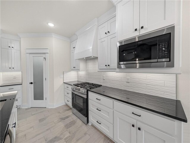 kitchen with white cabinets, custom exhaust hood, stainless steel appliances, and dark stone counters