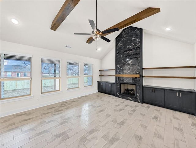 unfurnished living room with light wood-type flooring, vaulted ceiling with beams, a high end fireplace, and ceiling fan