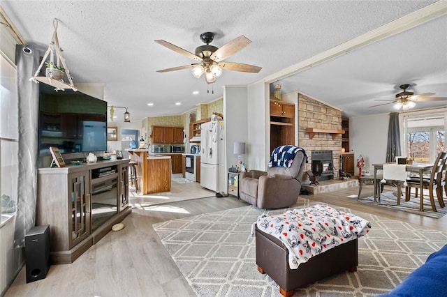 living room featuring a wood stove, lofted ceiling, light hardwood / wood-style flooring, ceiling fan, and a textured ceiling