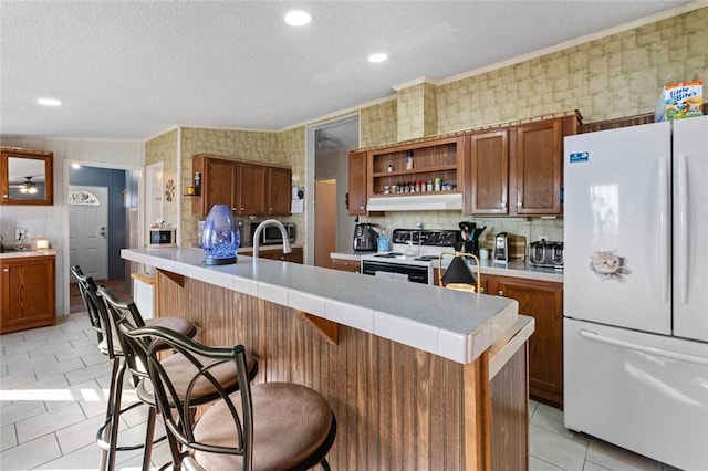 kitchen featuring a textured ceiling, white appliances, crown molding, light tile patterned floors, and a breakfast bar area