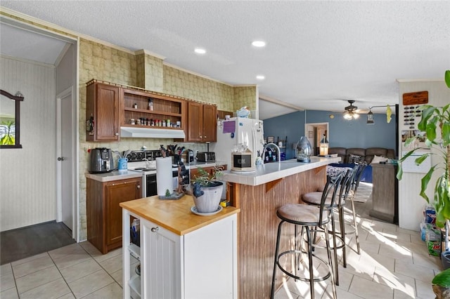 kitchen with ceiling fan, a kitchen breakfast bar, white refrigerator, a textured ceiling, and light tile patterned floors