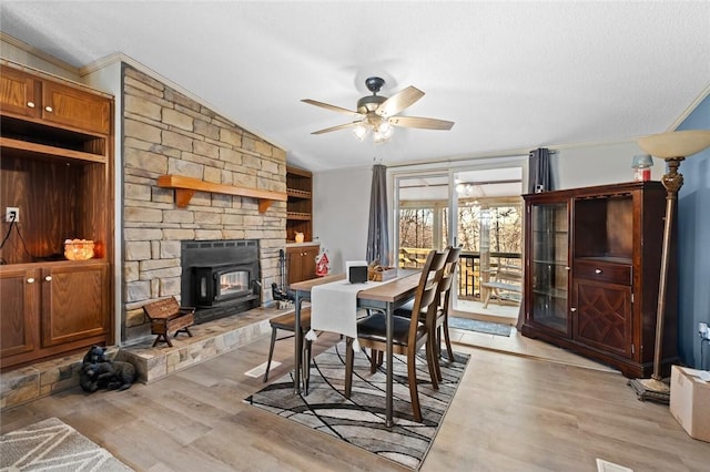 dining space with a wood stove, vaulted ceiling, ceiling fan, ornamental molding, and light hardwood / wood-style floors