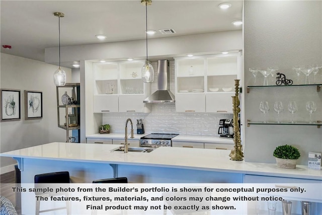 kitchen with pendant lighting, white cabinetry, high end stove, and wall chimney range hood