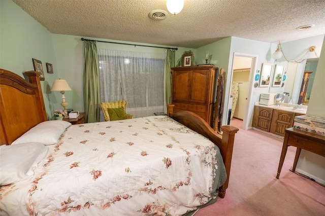 bedroom with ensuite bathroom, carpet, and a textured ceiling