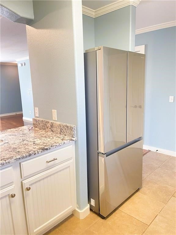 kitchen featuring crown molding, stainless steel fridge, light tile patterned flooring, light stone counters, and white cabinetry