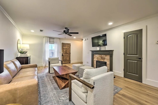 living room featuring ceiling fan, light wood-type flooring, ornamental molding, and a tiled fireplace