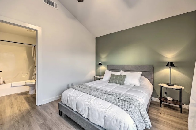 bedroom with connected bathroom, lofted ceiling, and hardwood / wood-style flooring