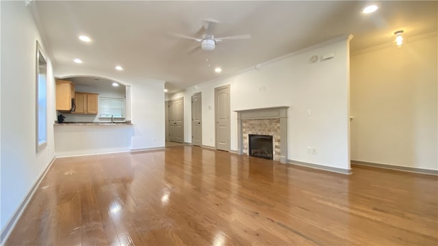 unfurnished living room with a stone fireplace, crown molding, ceiling fan, and wood-type flooring