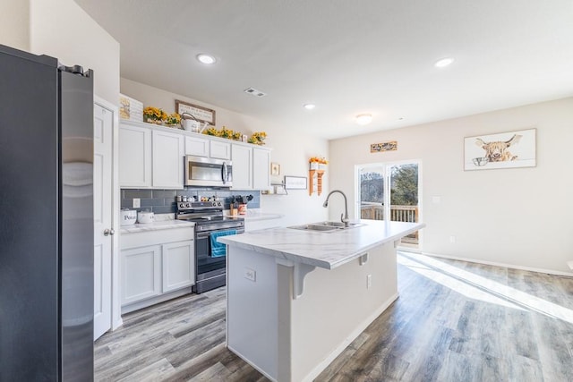 kitchen featuring decorative backsplash, light wood-type flooring, stainless steel appliances, sink, and white cabinetry