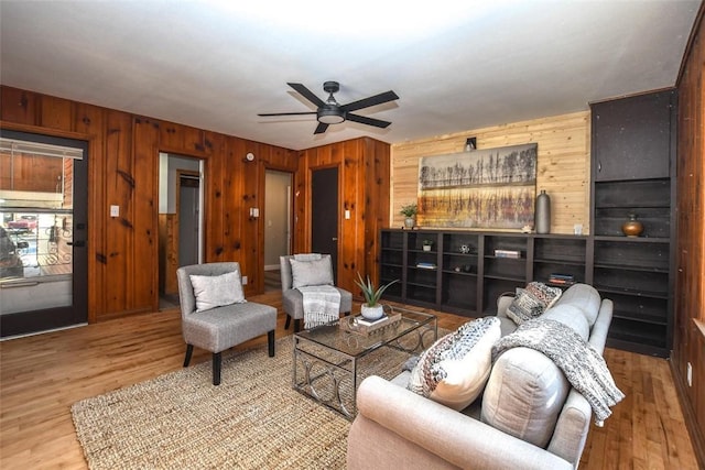 living room featuring wood-type flooring, ceiling fan, and wooden walls