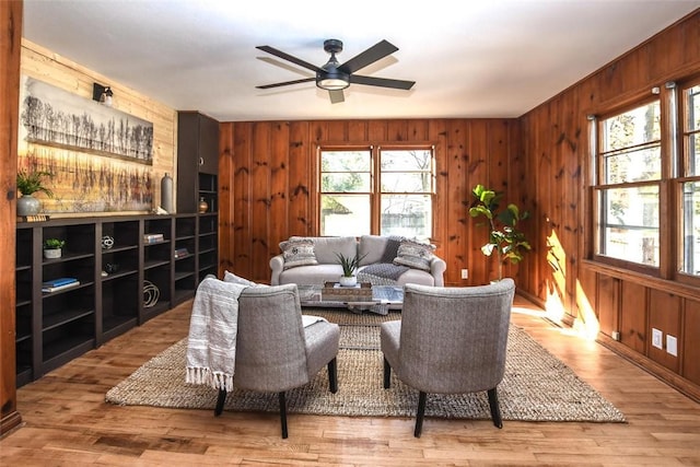 living room with hardwood / wood-style flooring, ceiling fan, and wood walls